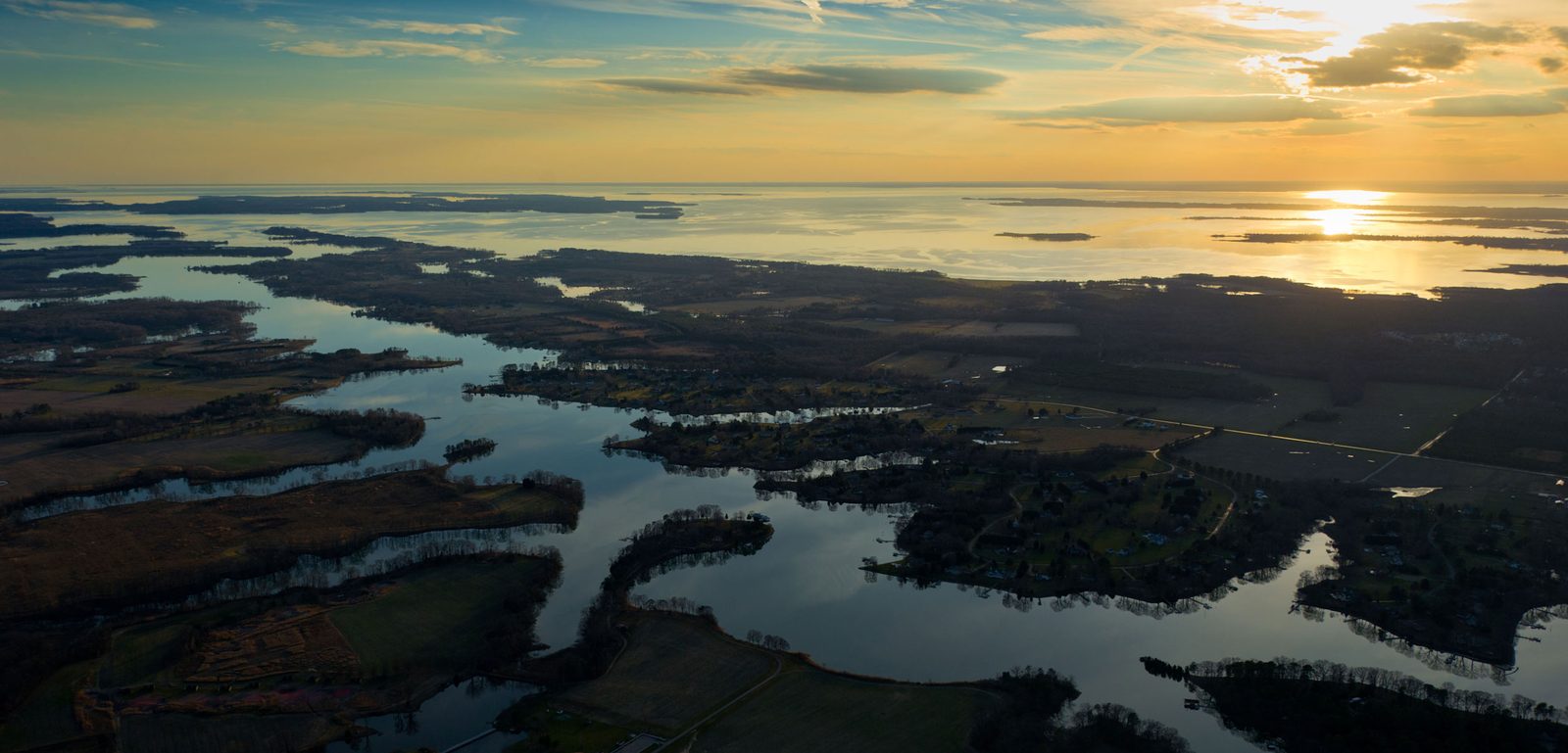 Aerial view of the Chesapeake Bay's Eastern Shore at sunset: winding tidal creeks, marsh and farmland opening onto the Bay.